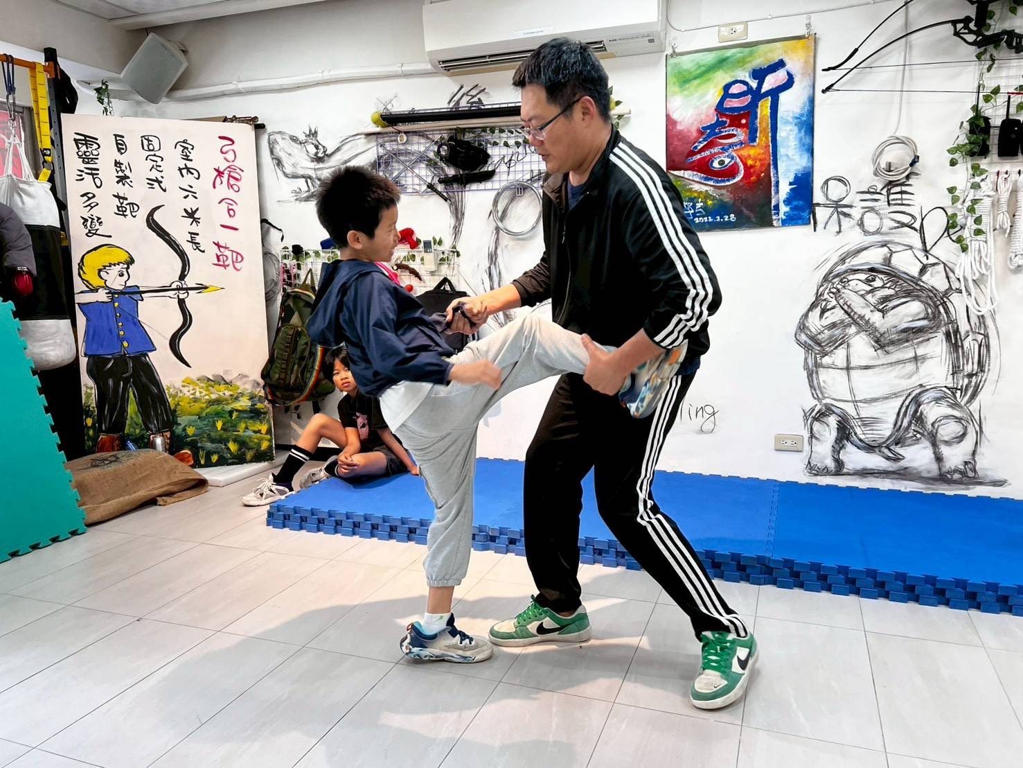 男孩抬腳往前踢,教練一手抓住他的腳踝、一手握著他的手
