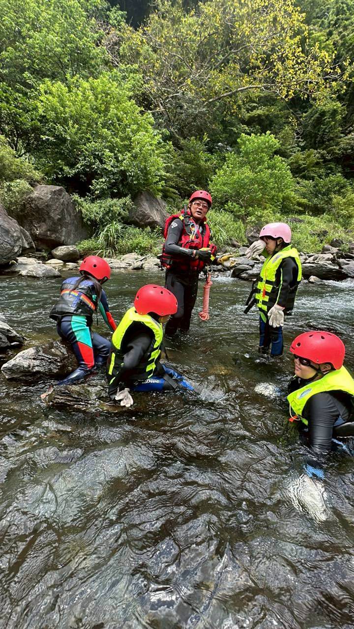 孩子戴安全帽、穿救生衣，在溪流中跟著大人練習