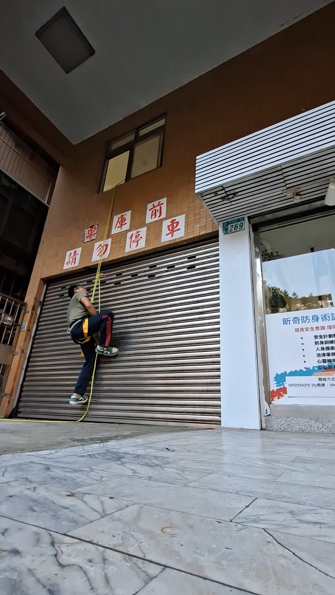中興路一段 269 號店門口，旁邊有人抓著繩子沿鐵捲門往上爬